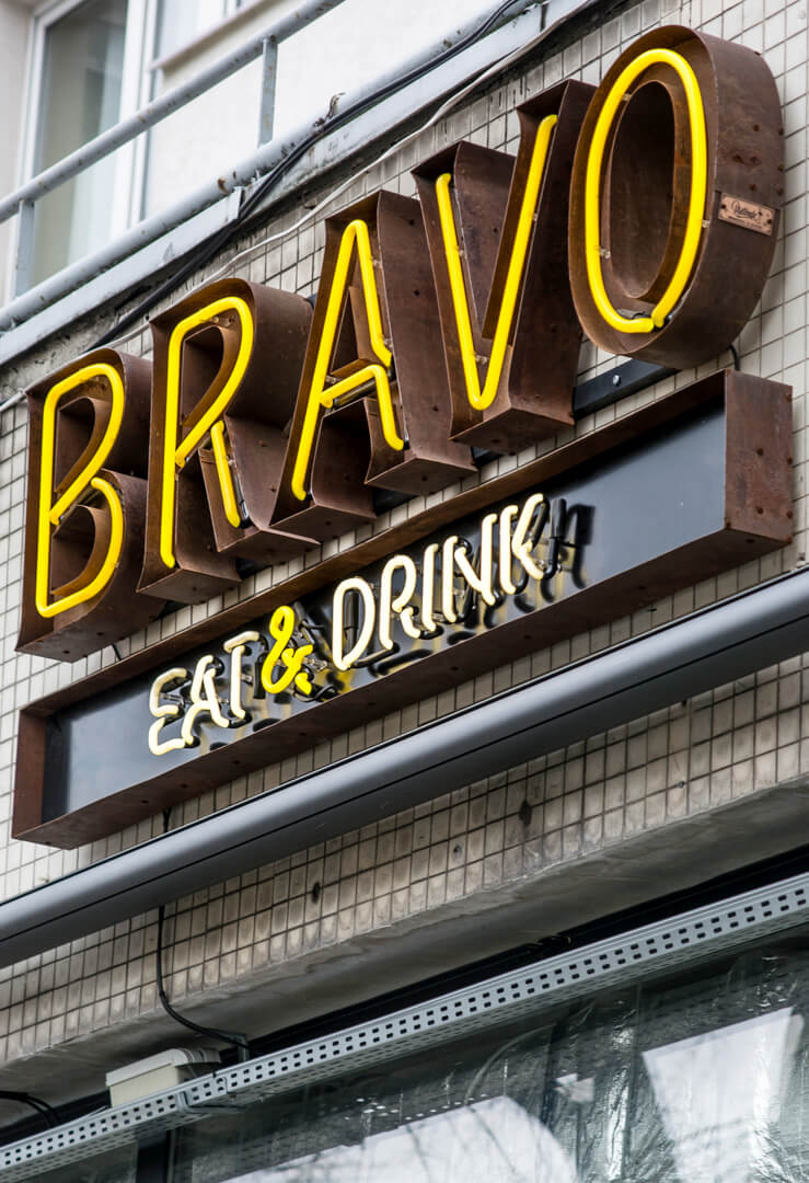 neon-bravo-eat-drink-neon-nad-wejsciem-do-restauracji-neon-na-kaflach-neon-na-scianie-z-kafli-neon-podswietlany-neon-wewnatrz-blachy-nierdzewnej-neon-na-zewnatrz-zolty-neon-warszawa-centralna